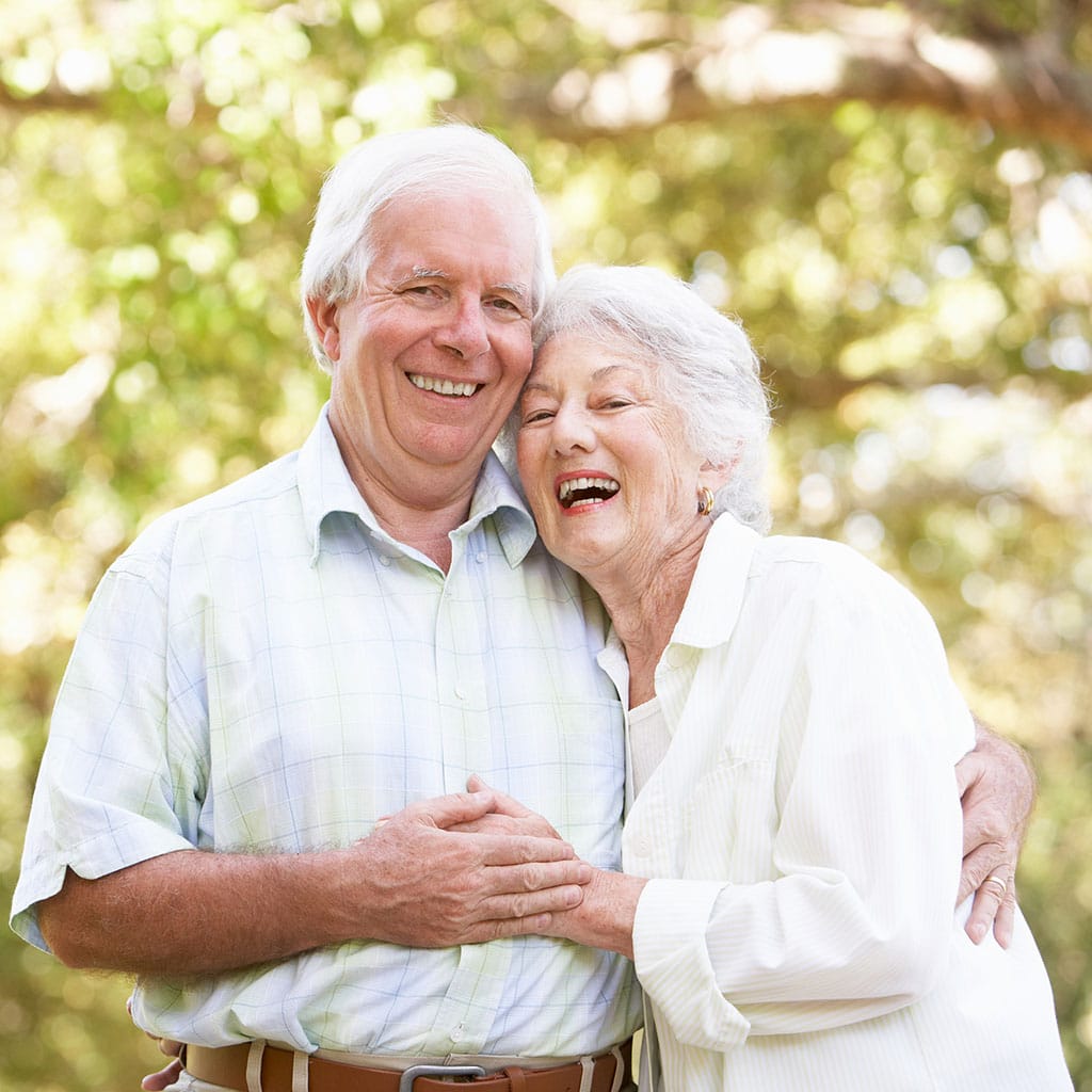 Smiling elderly couple embracing outdoors in a sunny setting